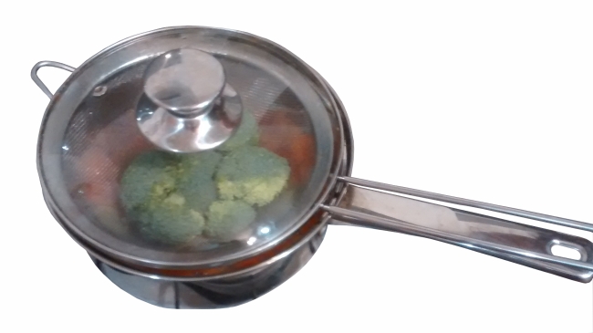 Photograph of a saucepan (containing carrots and potatoes) with a metal sieve full of broccoli inside